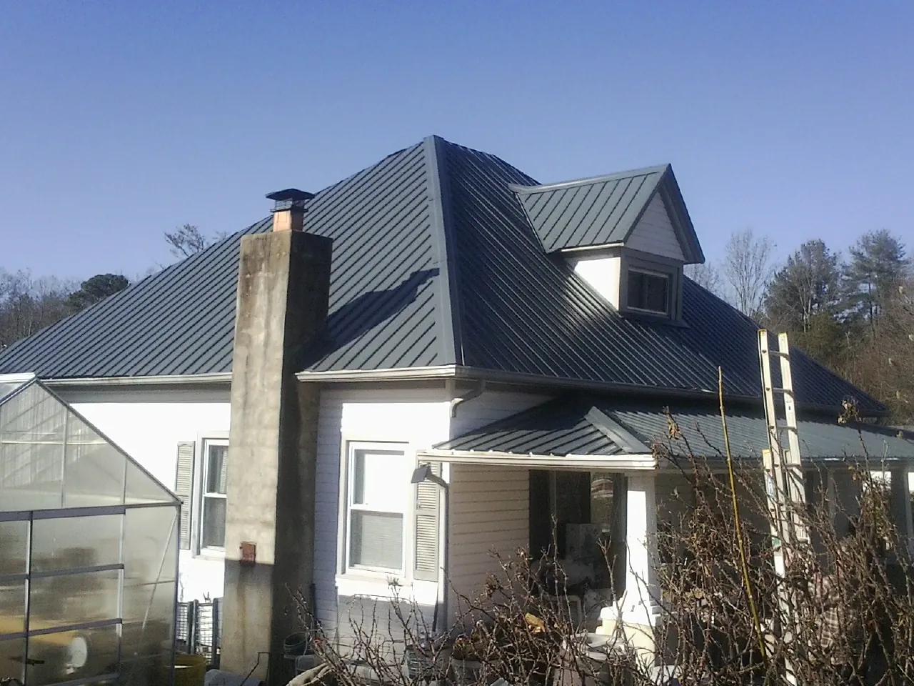 Dark blue standing seam metal roof on a white farmhouse with dormer — Slate & Tile Roof Repair by Roofing Brothers in Wessington