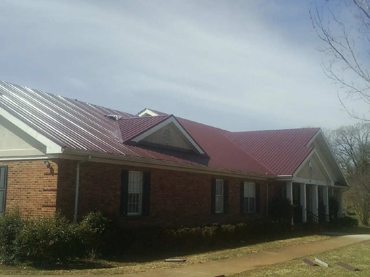 Red metal roof with gabled entries on a long brick building, from a Hail Damage Roof Repair job in Wessington