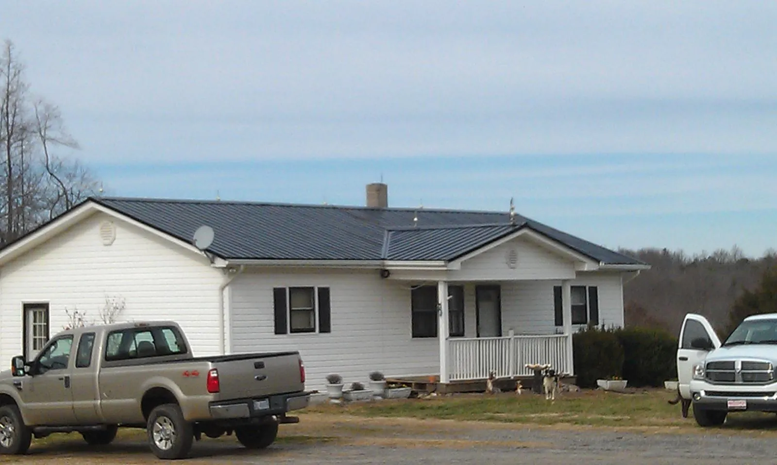Finished dark metal roof on a white ranch home with work trucks parked in Wessington