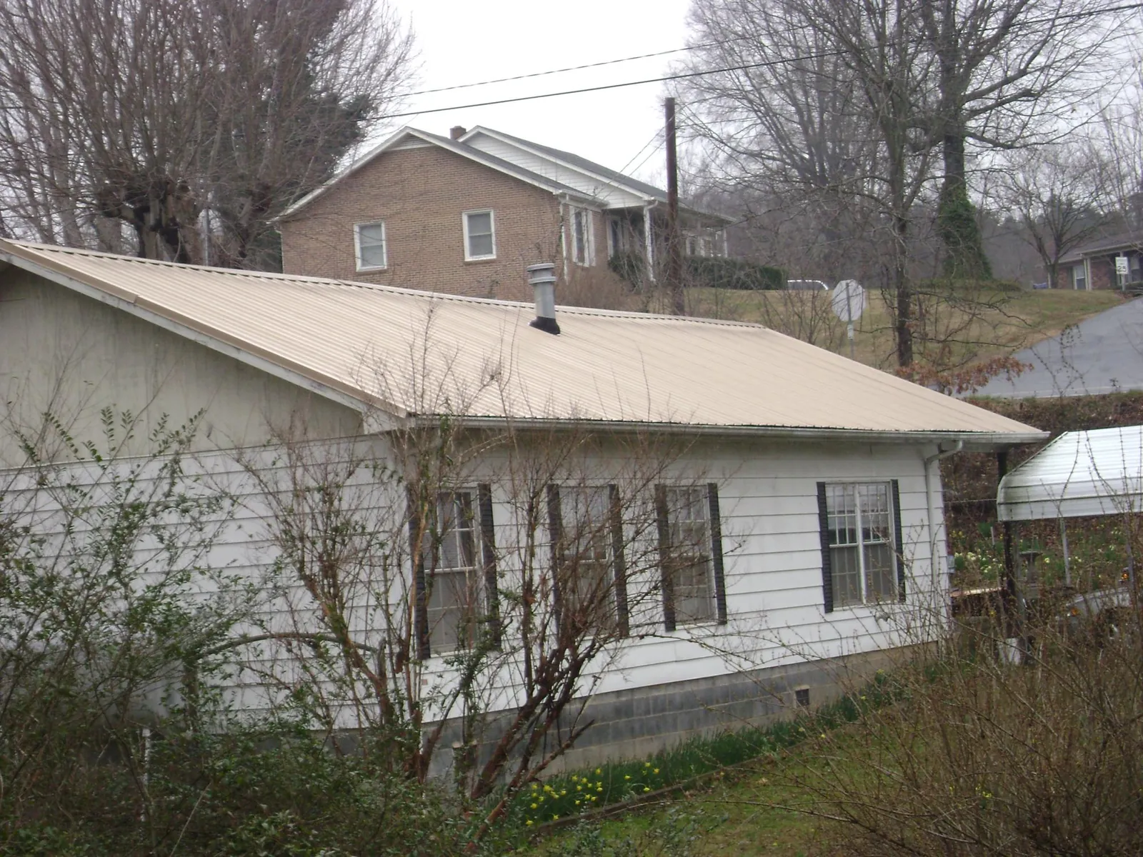 Tan metal roof on a white sided house set into a hillside — Commercial Roofing by Roofing Brothers in Wessington